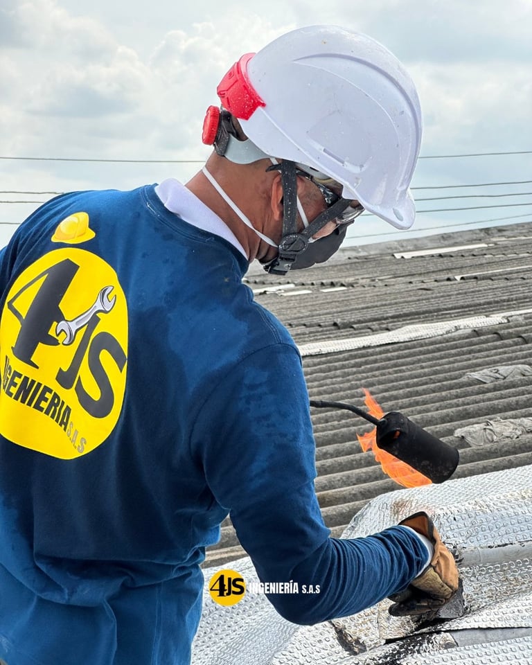 Worker in blue safety gear and white helmet inspecting roofing materials on an industrial roof