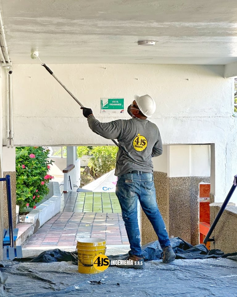 Construction worker in hard hat and safety vest scraping ceiling with long pole tool in unfinished building interior