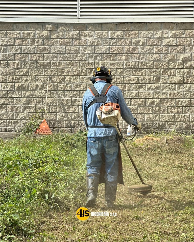 Worker in blue uniform and hard hat using a shovel to dig in a yard near a concrete block wall