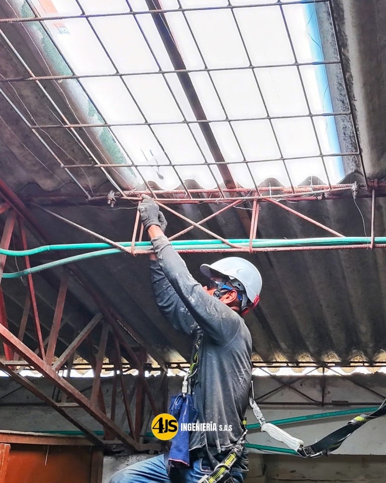 Construction worker in safety harness and hard hat installing blue cable on industrial steel framework with glass panels overhead